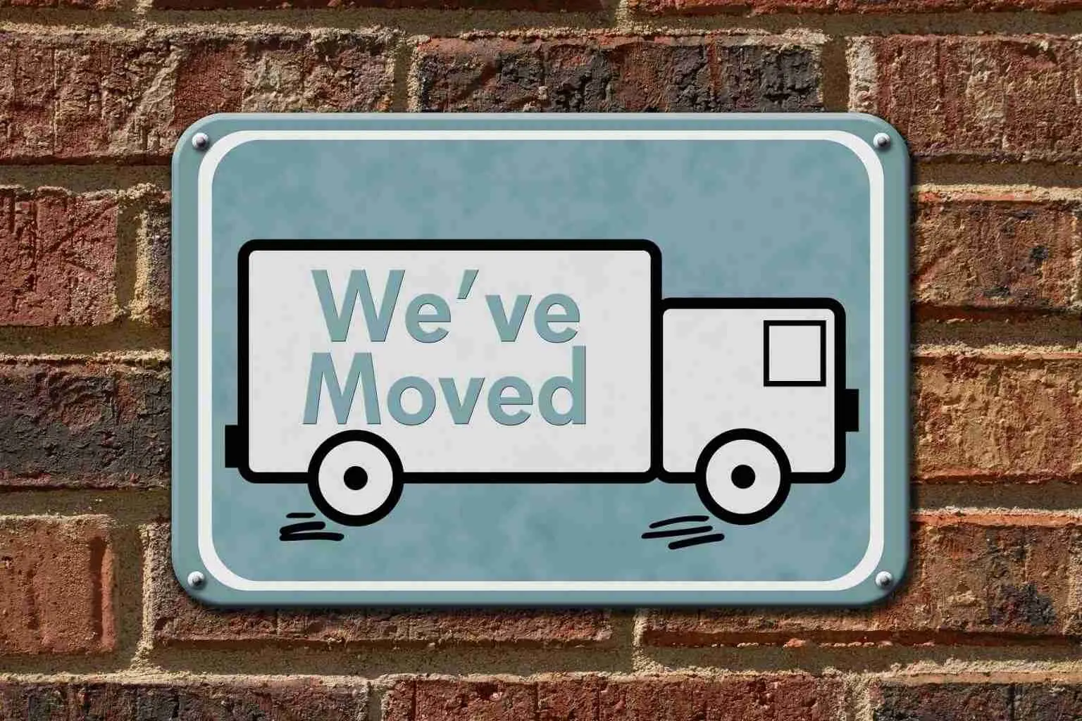 A sign with a cartoon moving truck and the words Weve Moved mounted on a brick wall.