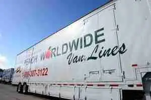 A large white moving truck with WORLDWIDE Van Lines and a phone number printed on its side, parked outdoors under a blue sky.
