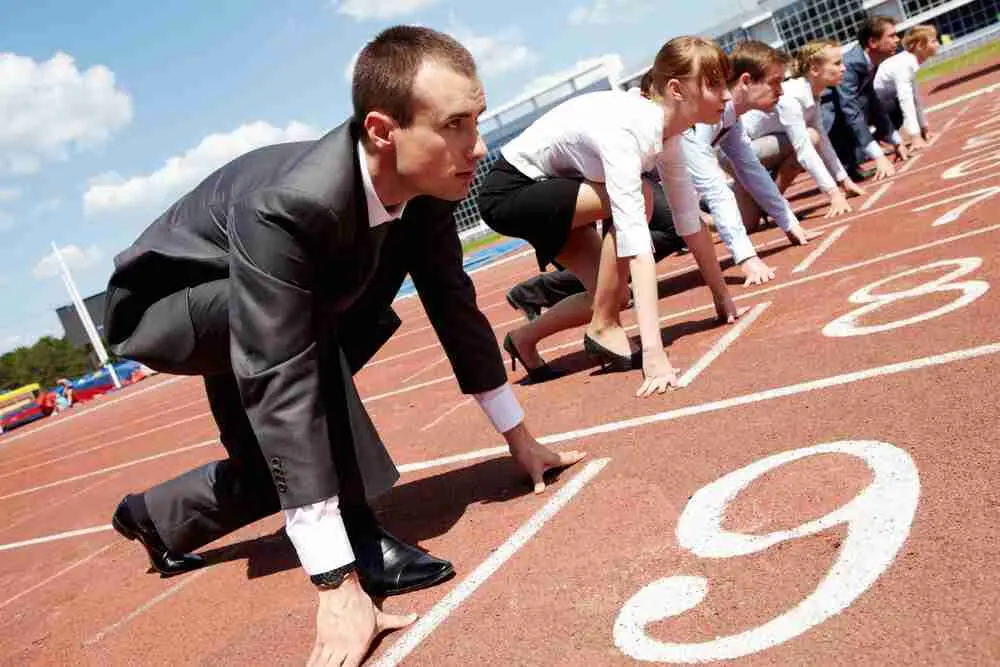 Several people wearing business attire crouch in starting positions on a running track, as if preparing for a race. The image combines professional and athletic themes.