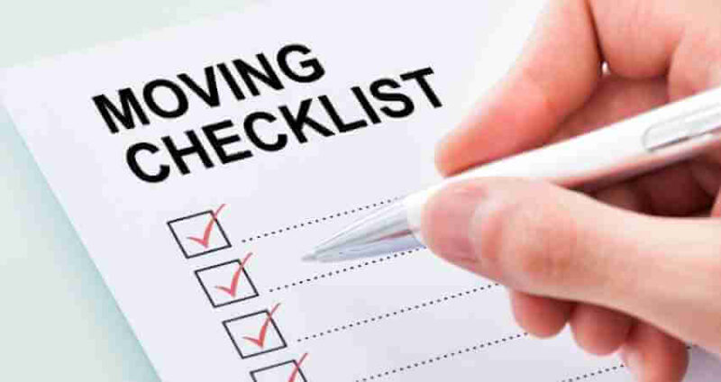 A hand holding a pen checks off boxes on a paper labeled MOVING CHECKLIST..
