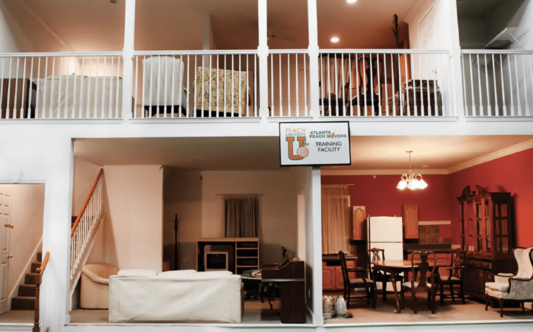 Two-story indoor facility with living and dining room furniture, white railings, and a sign reading Atlanta Peach U Training Facility above the lower level.