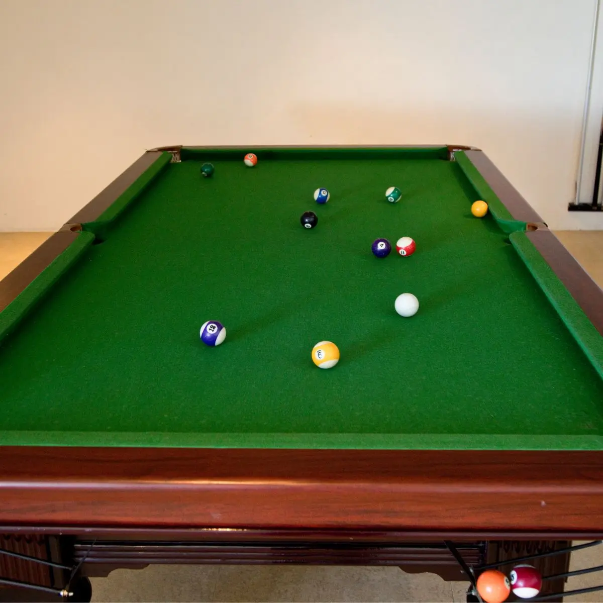 A green pool table with several colored balls scattered across the surface. The table has a wooden frame, and the balls include solids and stripes. The white cue ball is near the center.