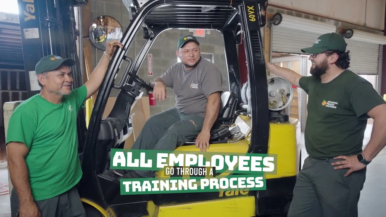 Three men in work uniforms stand and sit around a yellow forklift in a warehouse. Text on the image says, All employees go through a training process..